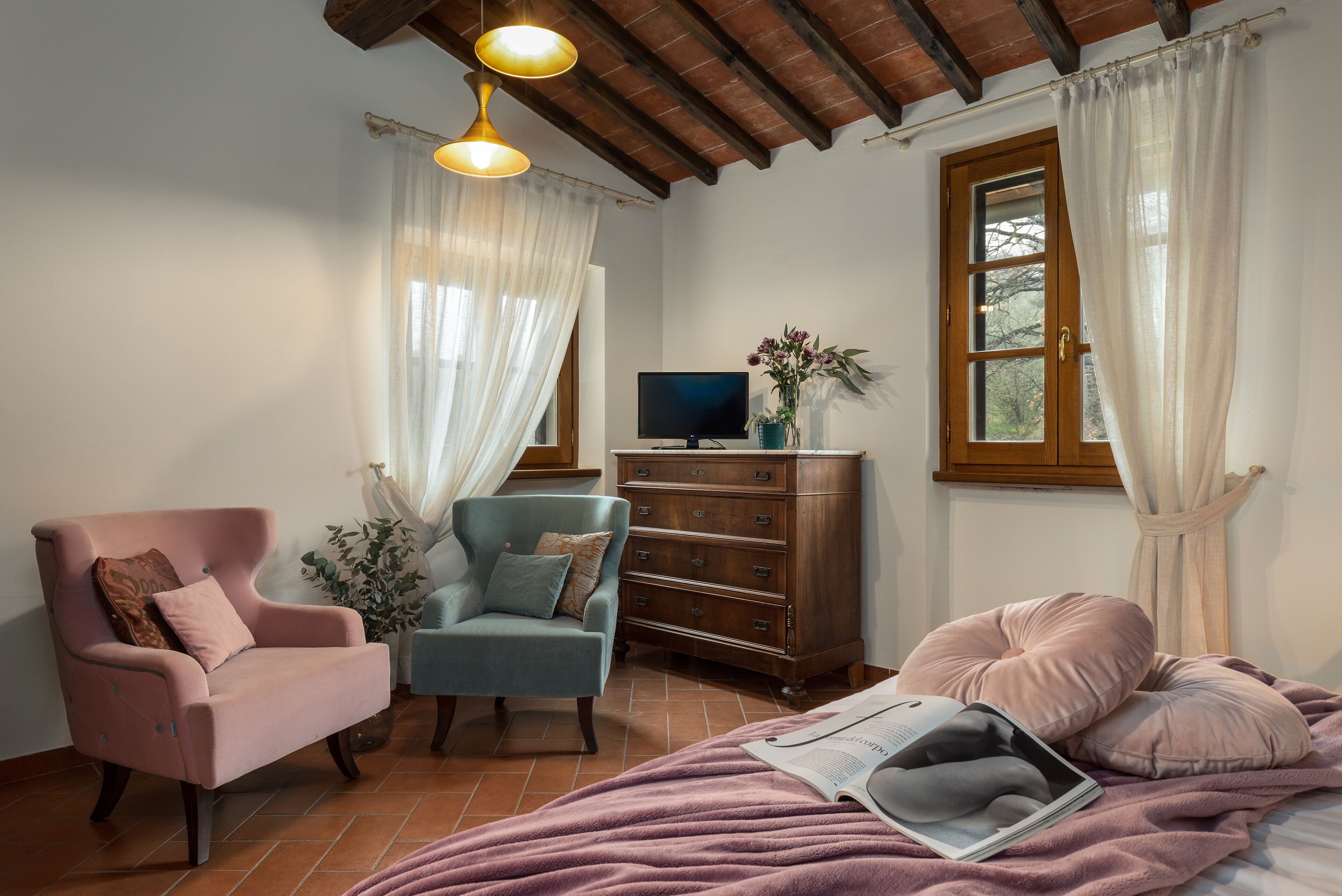 A cozy bedroom with a bed, two armchairs, a dresser, and a television.