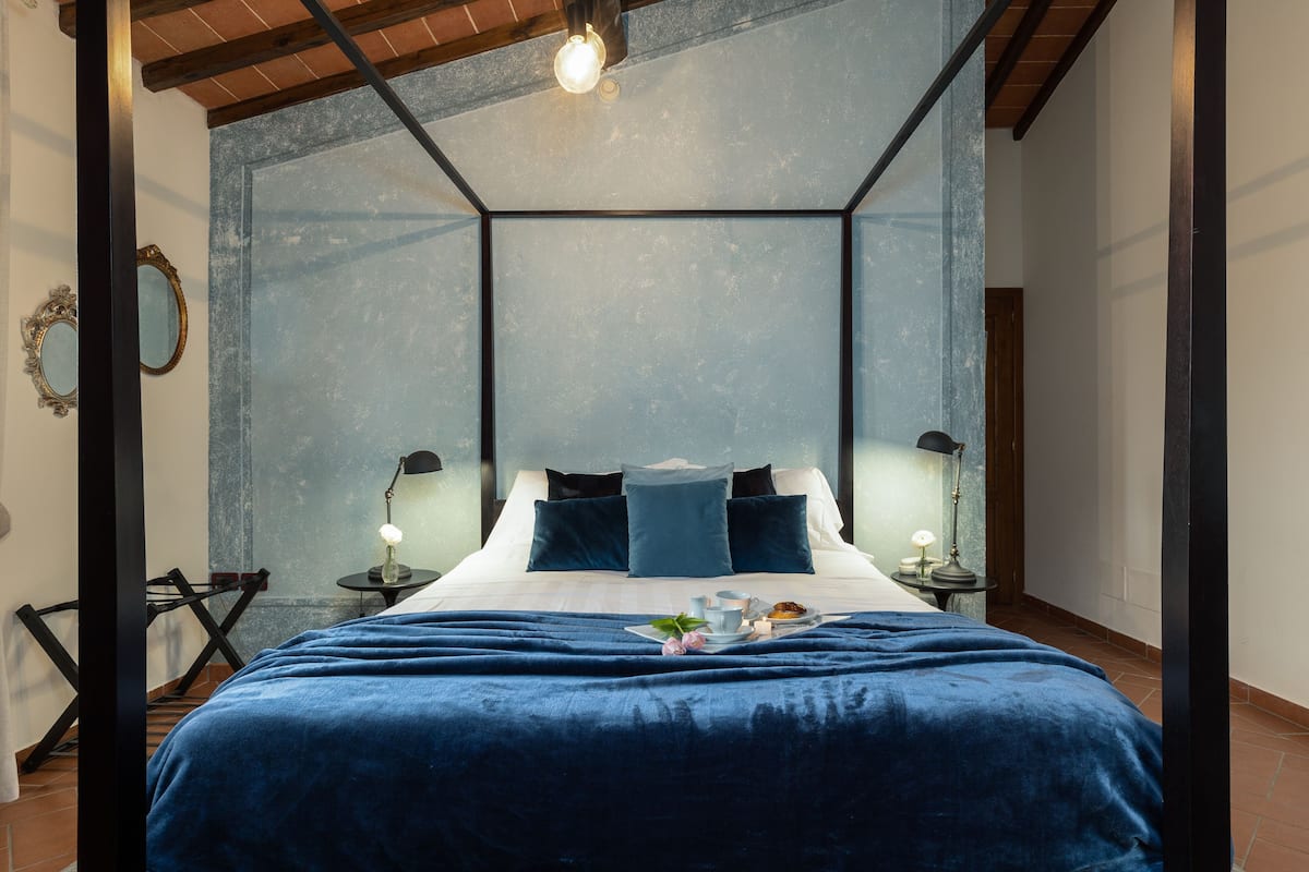 Une chambre moderne avec un grand lit, deux tables de chevet avec des lampes, une tête de lit bleue et une vue à travers un mur de verre.