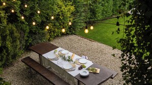 Een terras met een gedekte tafel voor een maaltijd, omgeven door groen en lichtjes.