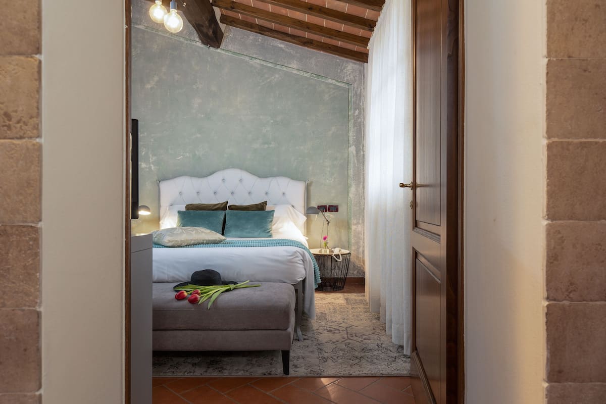 Une chambre à coucher avec un lit, une table de chevet, une lampe et une vue sur l’extérieur, visible à travers une porte ouverte.