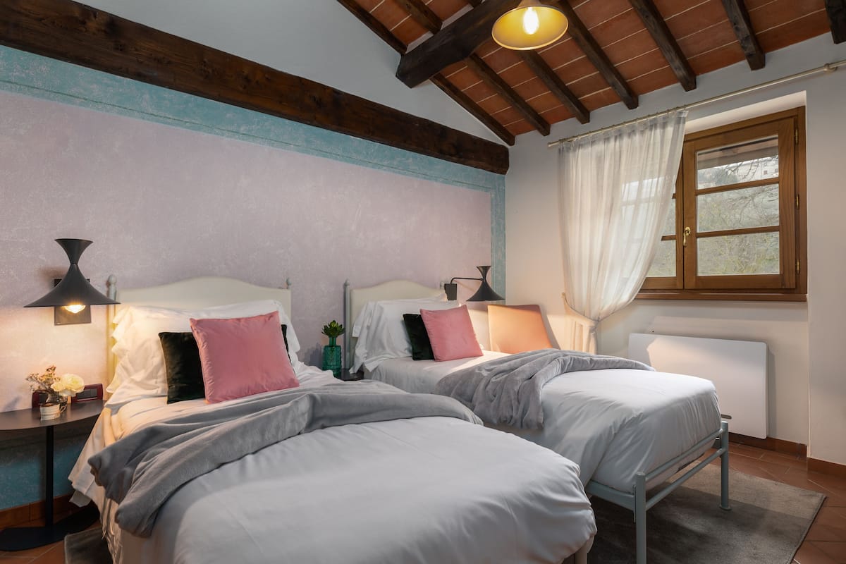 Une chambre avec deux lits, un plafond en bois, une fenêtre avec des rideaux et des lampes de chevet.