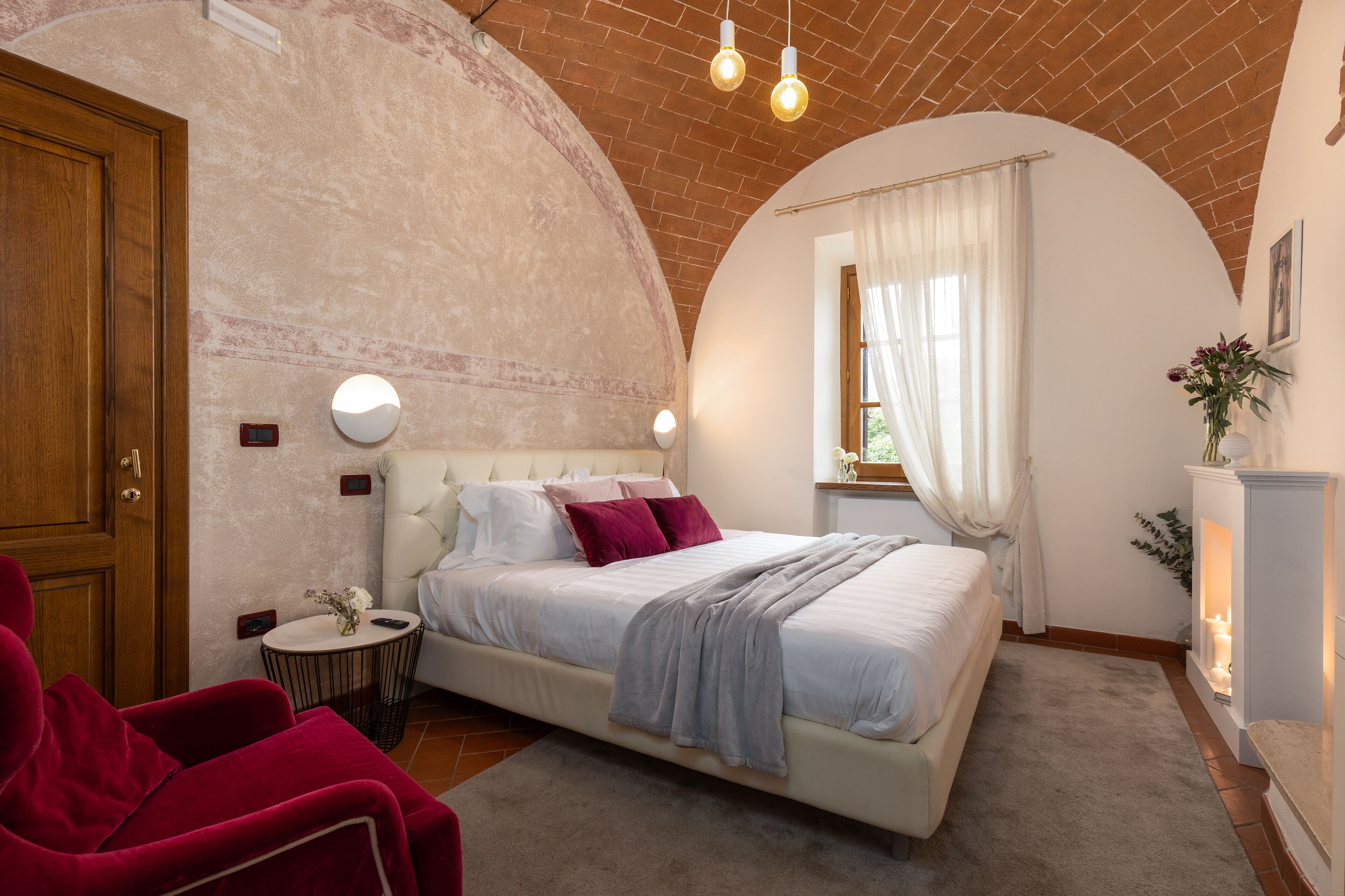 A bedroom with a large bed, a red chair, a round side table, and a fireplace.