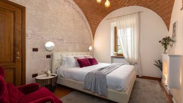 A bedroom with a large bed, a red chair, a round side table, and a fireplace.
