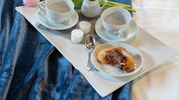 A tray with a cup of tea, a small bowl of jam, a spoon, and a tulip on a bed with a blue blanket.