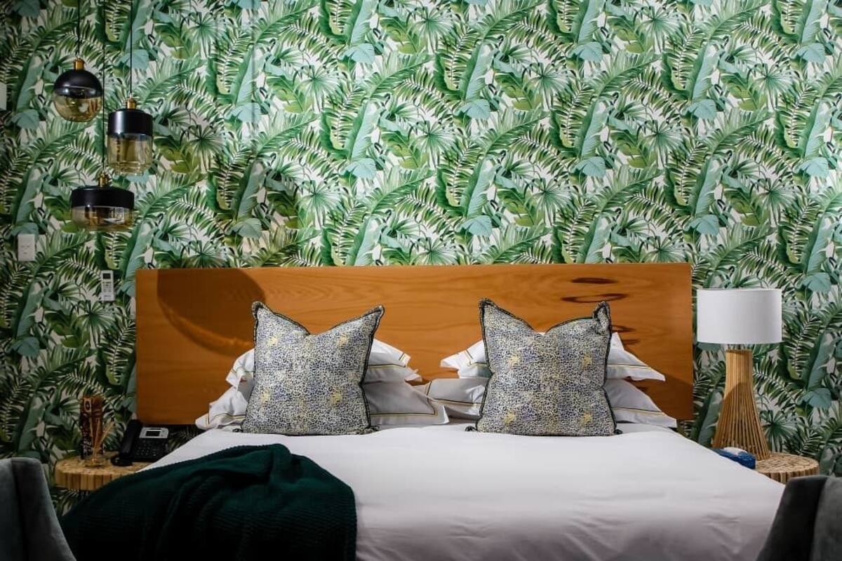 A hotel room with a bed, a wooden headboard, patterned wallpaper, a bedside lamp, and a telephone on a side table.