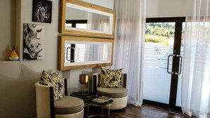 A modern living room with two armchairs, a coffee table, and a large mirror. There is a door leading outside with a view of a parking lot. - eMfuleni Lifestyle (Lobamba)