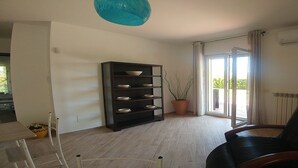 A living room with a black chair, a bookshelf, a potted plant, and a sliding glass door to a balcony. - Villa Aurelio (Squillace)