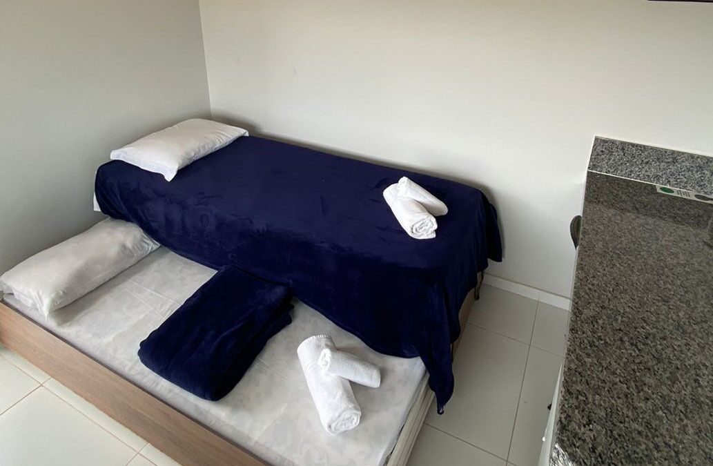 A single bed with a dark blue bedspread and white pillows, a wooden headboard, and a small step leading up to the bed.