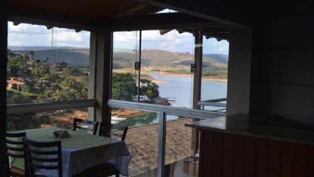Un balcón con una mesa y sillas, con vistas a un paisaje pintoresco con colinas y una masa de agua.
