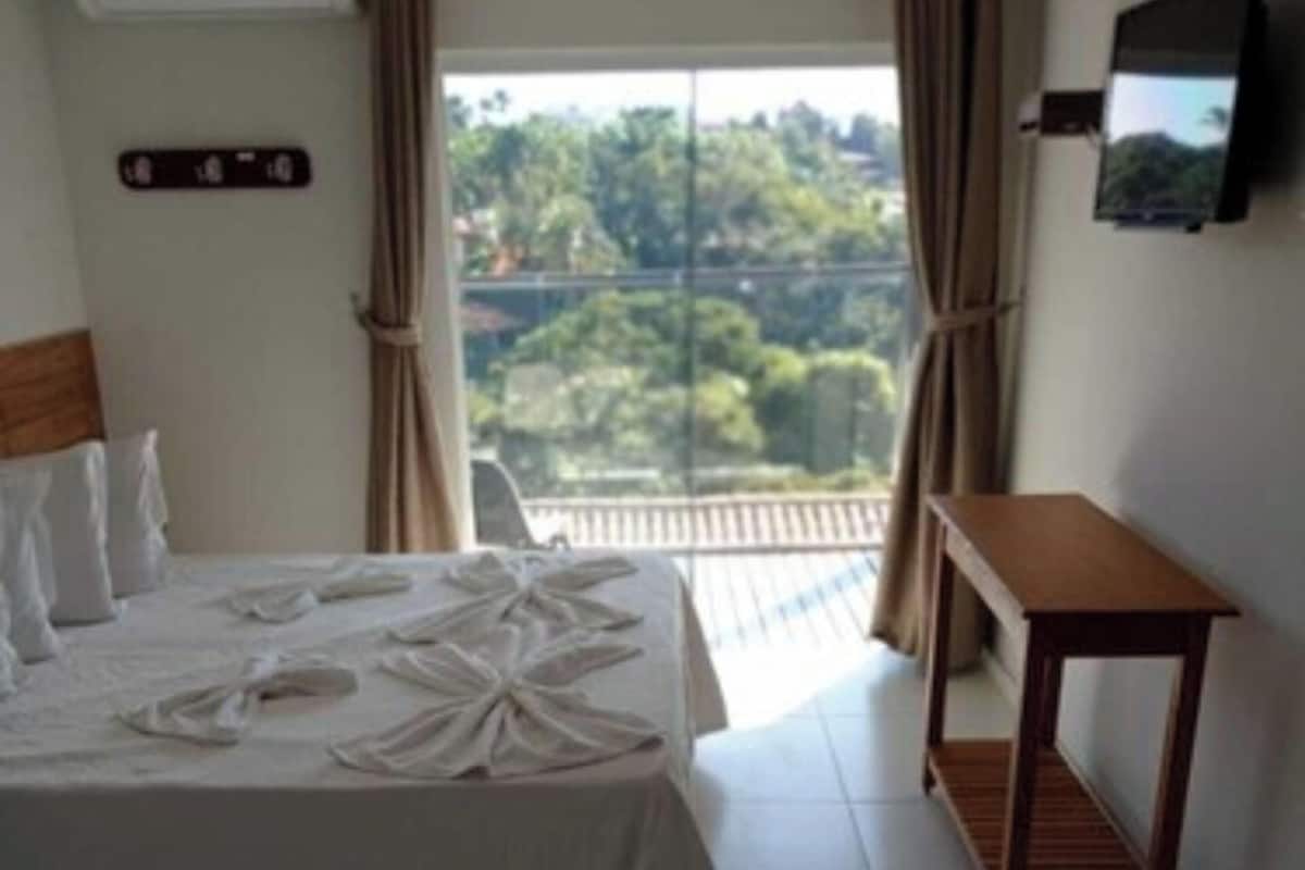 A hotel room with a bed, a small table, a TV, and a window with curtains.
