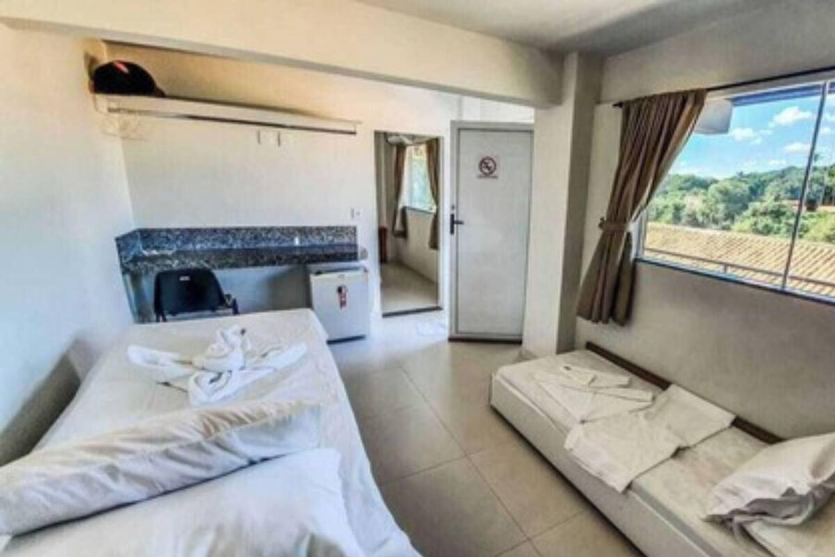 A hotel room with a bed, a sofa, a small table, a window with a view, and a door leading to a bathroom.