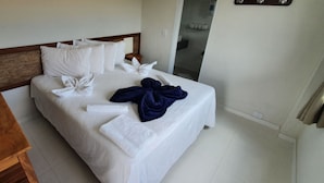 Una cama bien hecha con sábanas blancas, un cabecero de madera y toallas dispuestas sobre la cama.