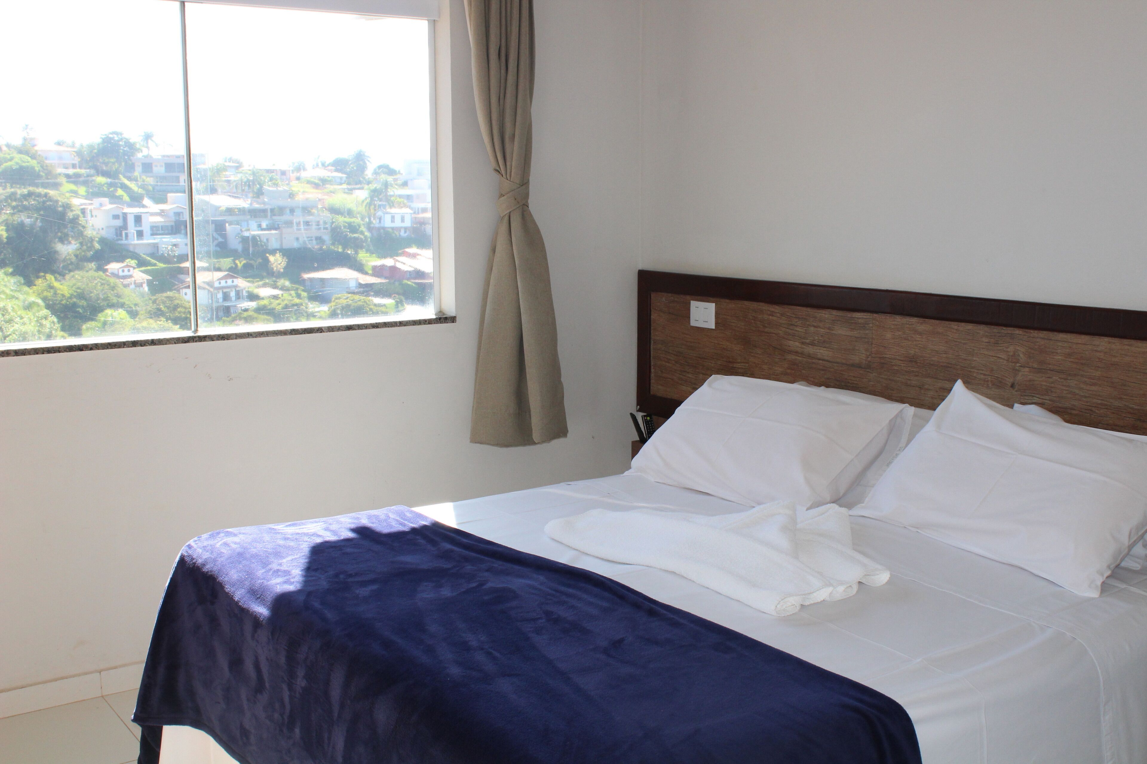 Ein Hotelzimmer mit Bett, Blick auf die Stadt durch ein Fenster und einem Vorhang.