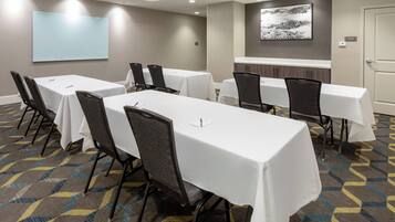 Un salón de conferencias con mesas y sillas blancas, una pantalla de proyector y un área de almacenamiento.