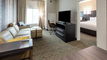 A hotel room with a sofa, a desk, a television, and a bed.