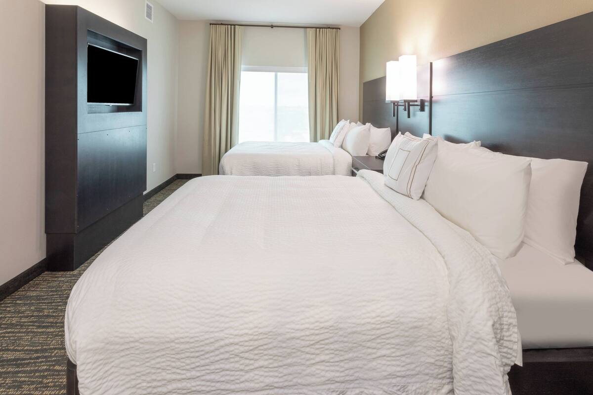 A hotel room with a large bed, a TV mounted on the wall, and a window with curtains.