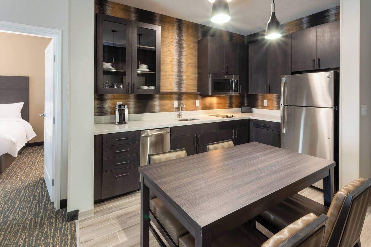 A modern kitchen with dark wood cabinets, stainless steel appliances, and a wooden dining table.