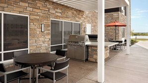 Un patio al aire libre con muro de piedra, una parrilla, una mesa con sillas y una zona de estar techada.