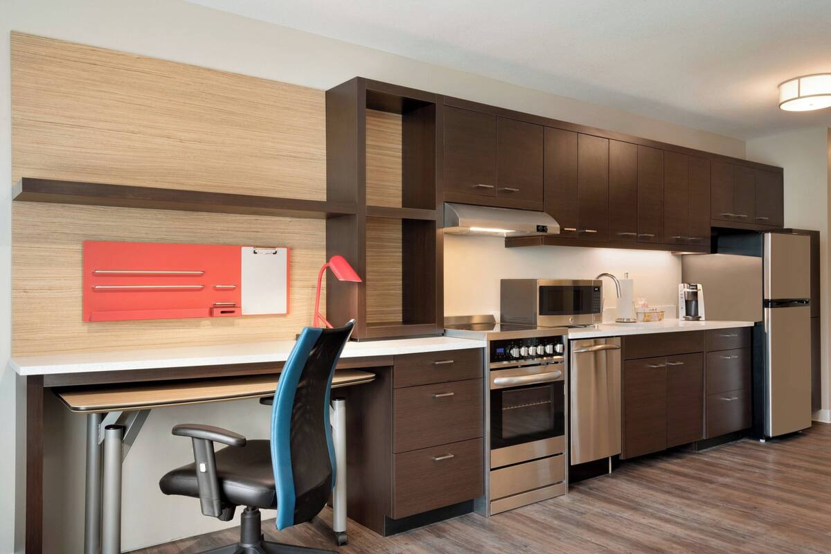 A modern kitchen with wooden cabinets, a stainless steel refrigerator, a microwave, and a built-in oven.