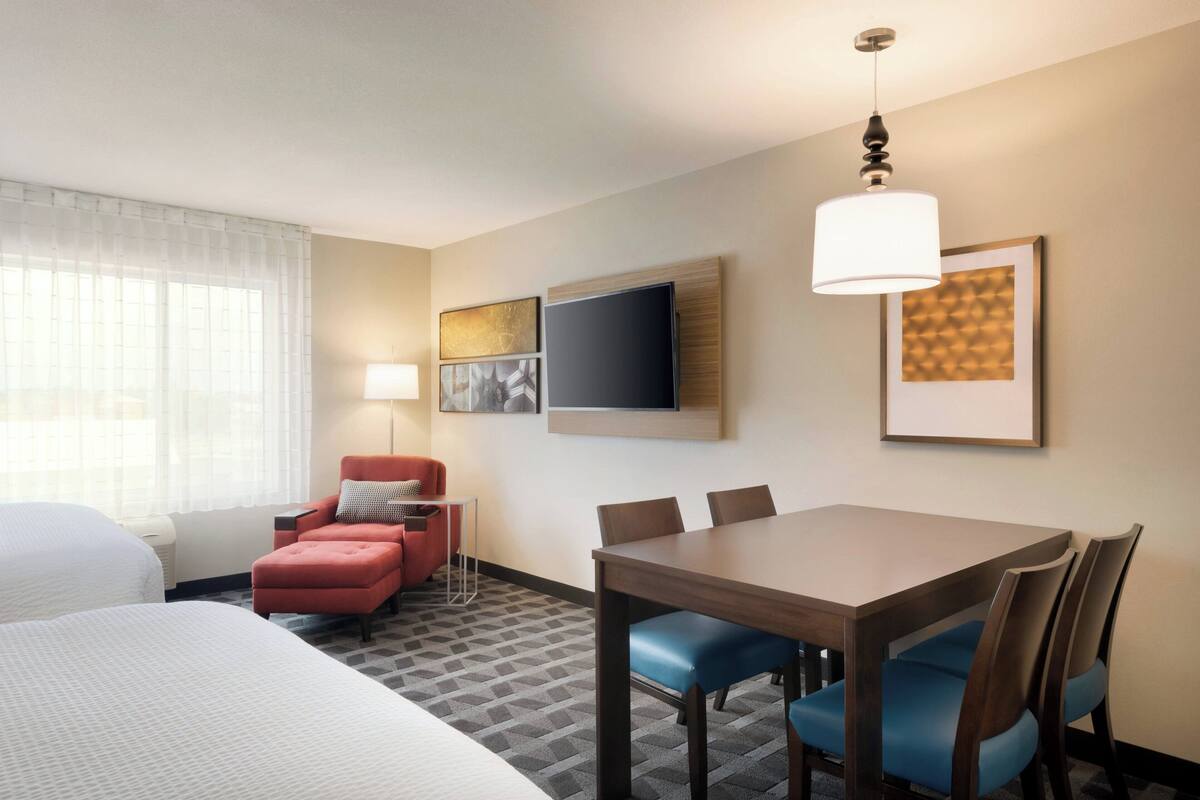 A hotel room with a bed, a desk, a chair, a television, and a lamp.