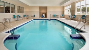 Una piscina interior con agua azul cristalina, rodeada de sillones y mesas, y grandes ventanales en un lateral.
