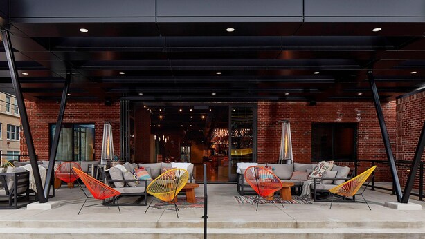 An outdoor seating area with modern chairs and a sofa, a brick building in the background, and a covered entrance. - Moxy Chattanooga Downtown (Chattanooga)