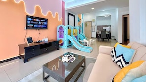 A modern living room with a flat-screen TV, a sofa with colorful cushions, a coffee table, and a children's play area with a slide.