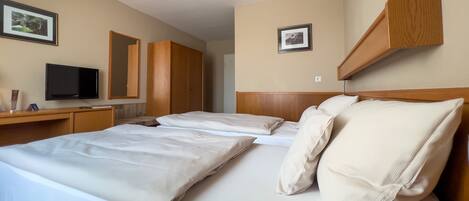 Habitación de hotel con dos camas, un escritorio con televisor de pantalla plana, armario de madera y cuadros en las paredes.