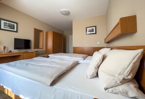 A hotel room with two beds, a desk with a flat-screen TV, wooden wardrobe, and framed pictures on the walls.