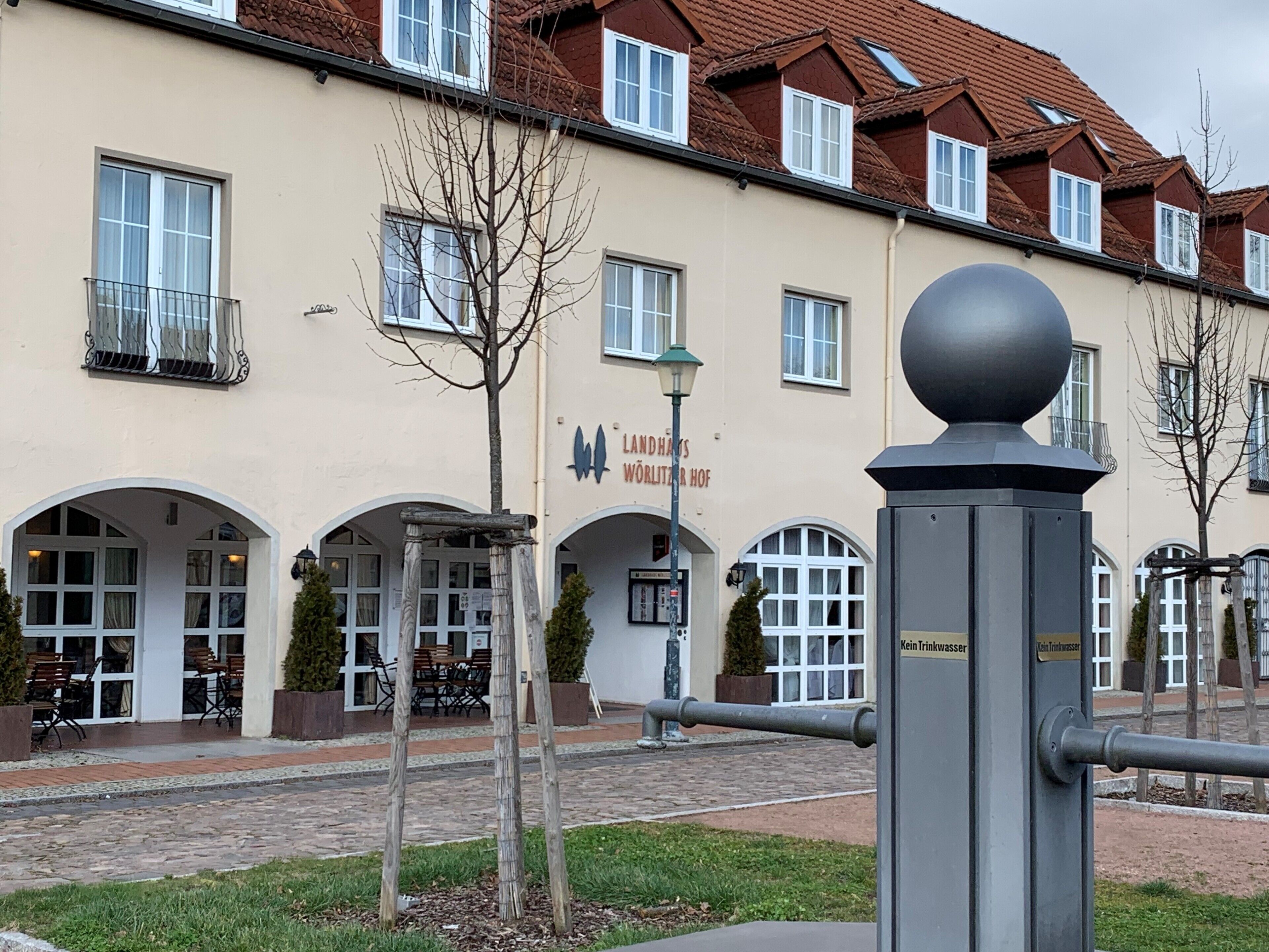 A building with a sign reading "Landhaus Wörlitzer Hof" and a water fountain in the foreground.