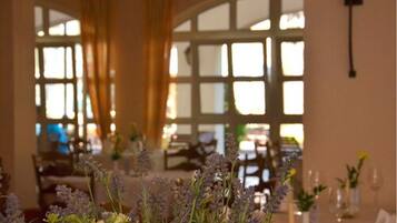 Een binnen restaurantgedeelte met gedekte tafels, een groot raam met gordijnen en uitzicht op buiten.