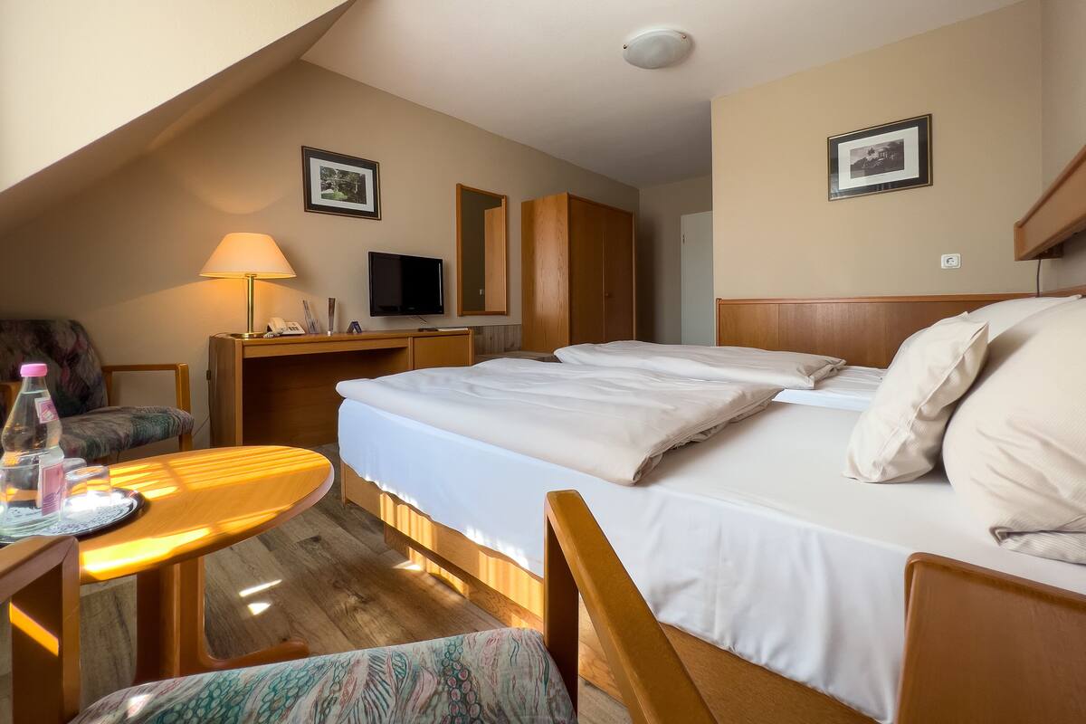 A hotel room with a bed, a desk with a lamp, a chair, and a television.