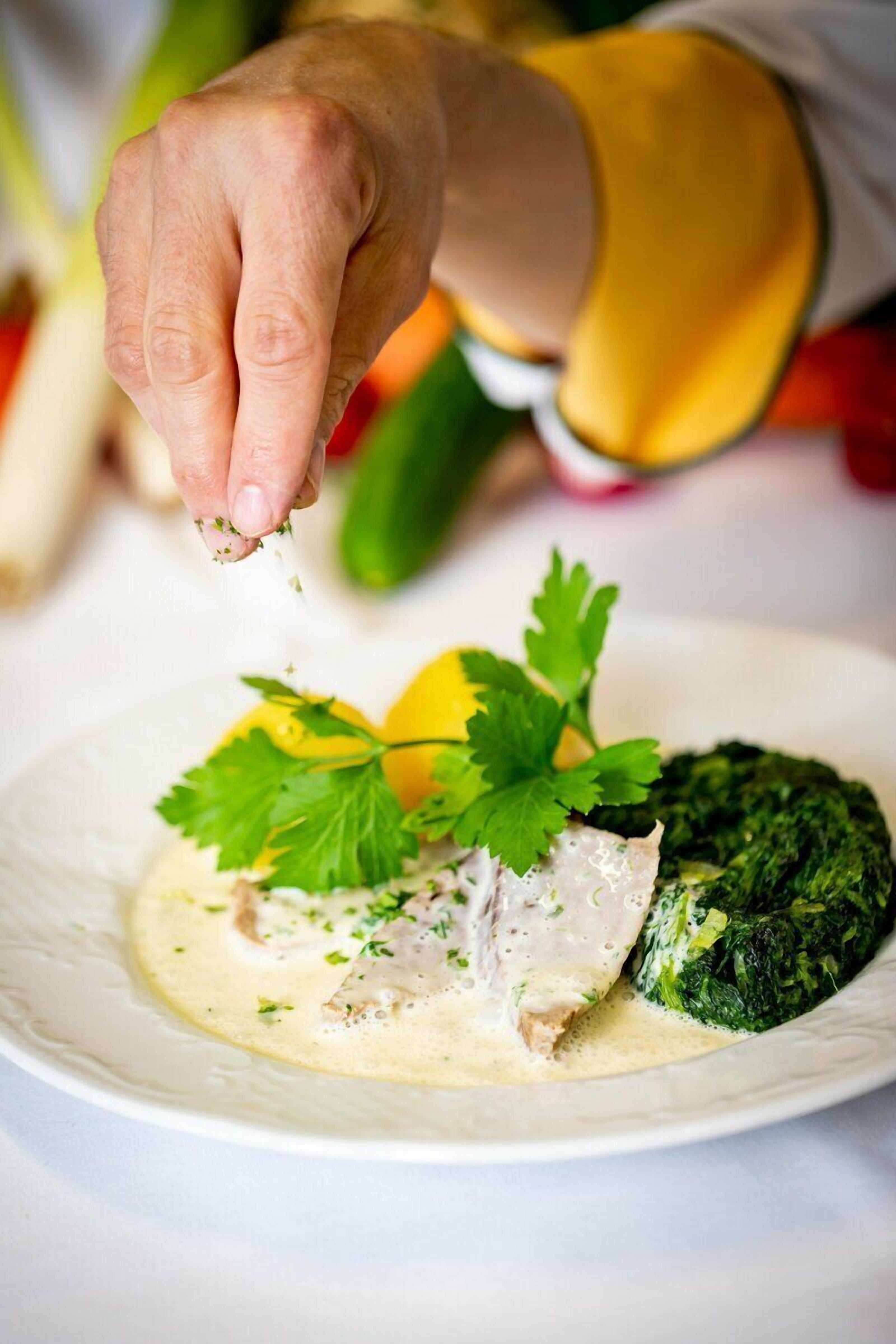 Una mano esparciendo hierbas sobre un plato con pescado y verduras.