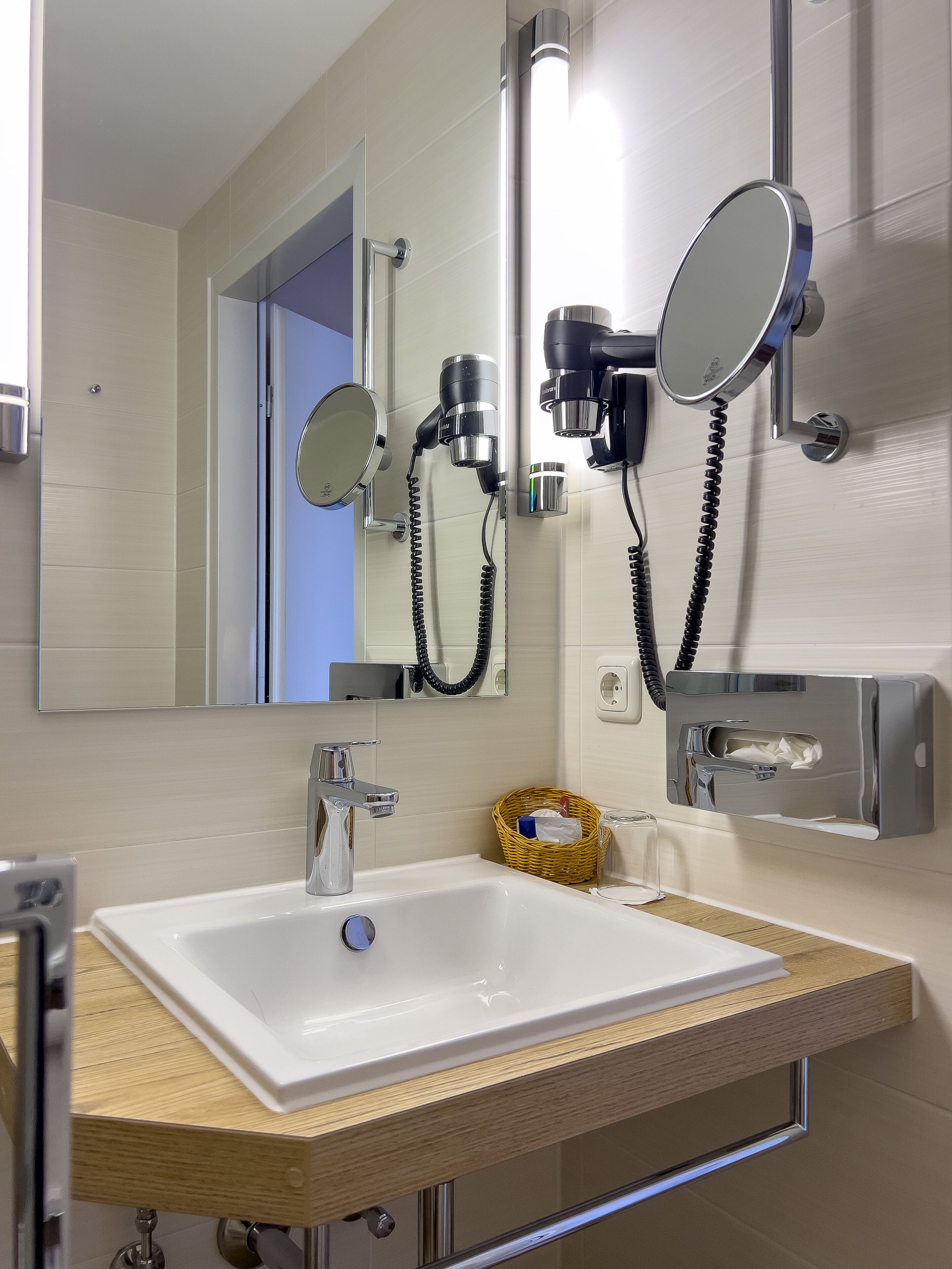 A bathroom with a white sink, chrome fixtures, a mirror, and a hairdryer mounted on the wall.