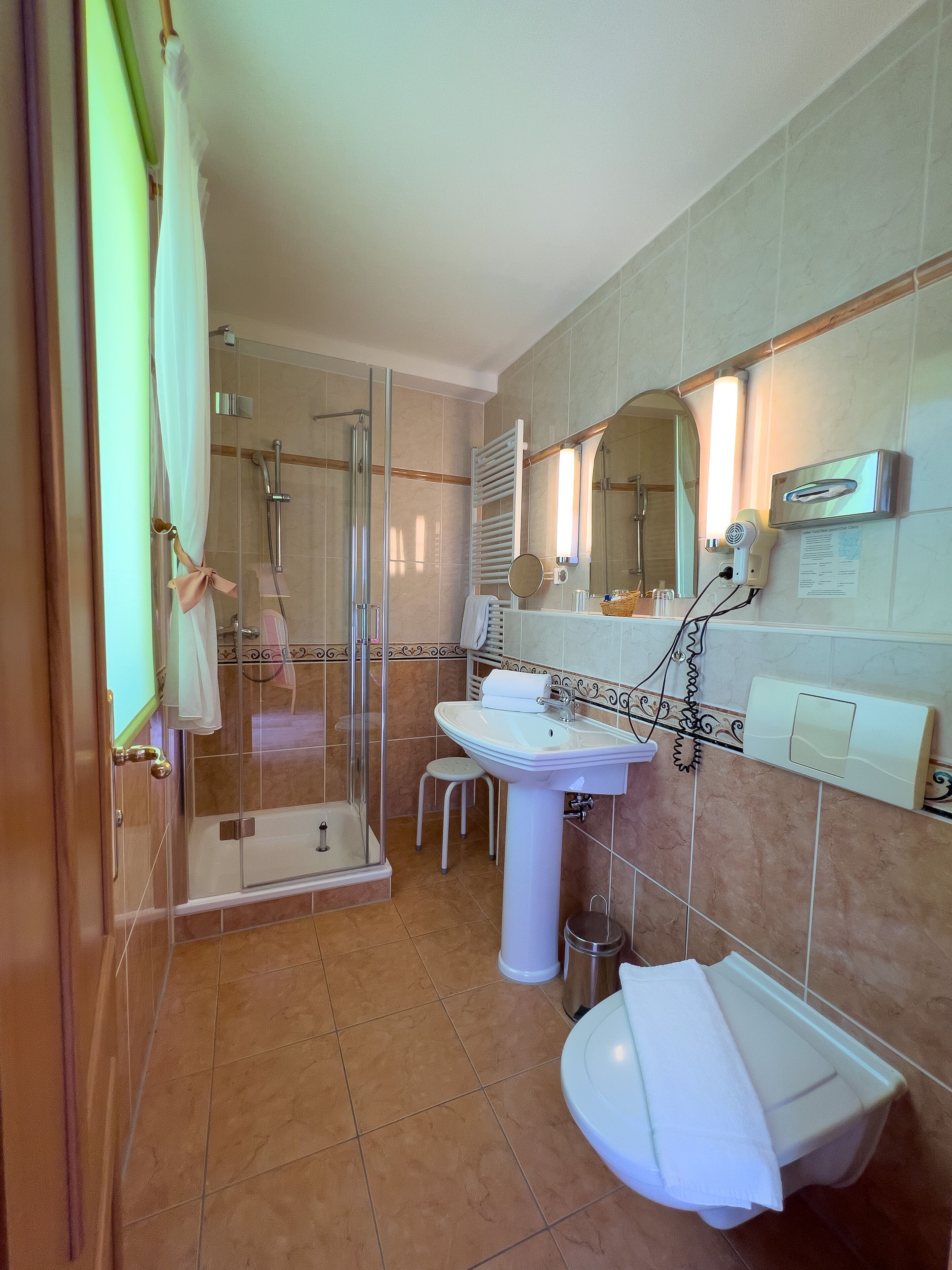 A modern bathroom with a glass-enclosed shower, a pedestal sink, and a vanity mirror.