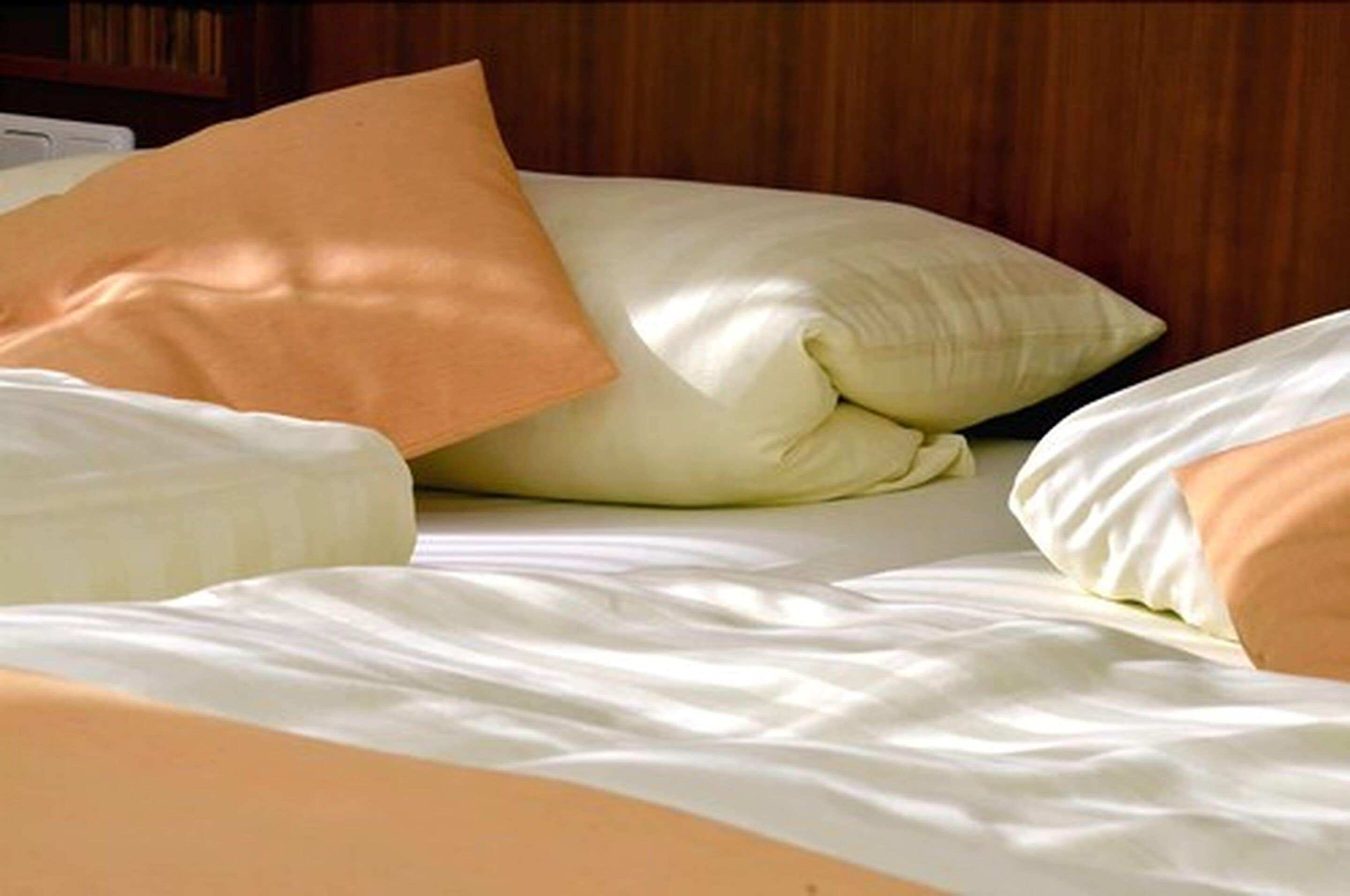 Una cama con ropa de cama blanca y color melocotón, incluyendo almohadas y edredón.