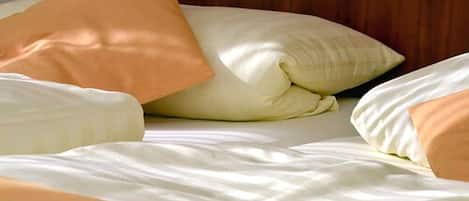 Una cama con ropa de cama blanca y color melocotón, incluyendo almohadas y edredón.