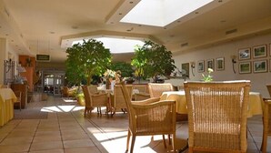 A spacious indoor area with high ceilings, natural light from skylights, wicker furniture, and potted plants. - Hotel Landhaus Wörlitzer Hof (Oranienbaum-Wörlitz)