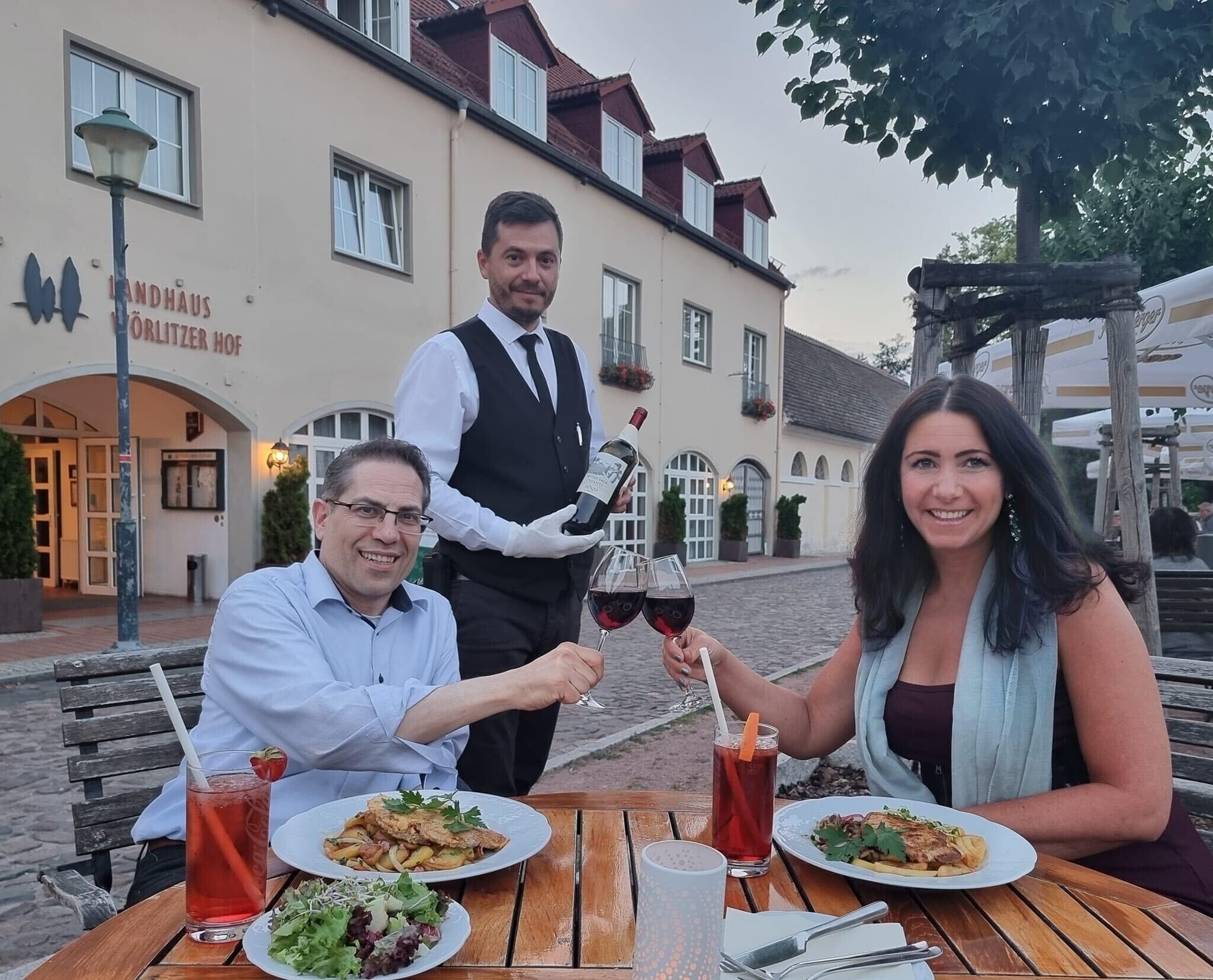 Un restaurante con terraza, un camarero sirviendo vino y comensales disfrutando de sus comidas.