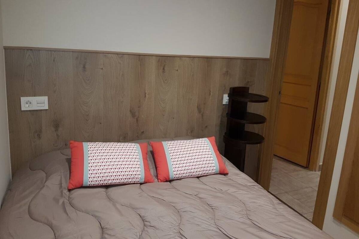 A bedroom with a wooden headboard, a bed with patterned pillows, a bedside table, and a door leading to another room.