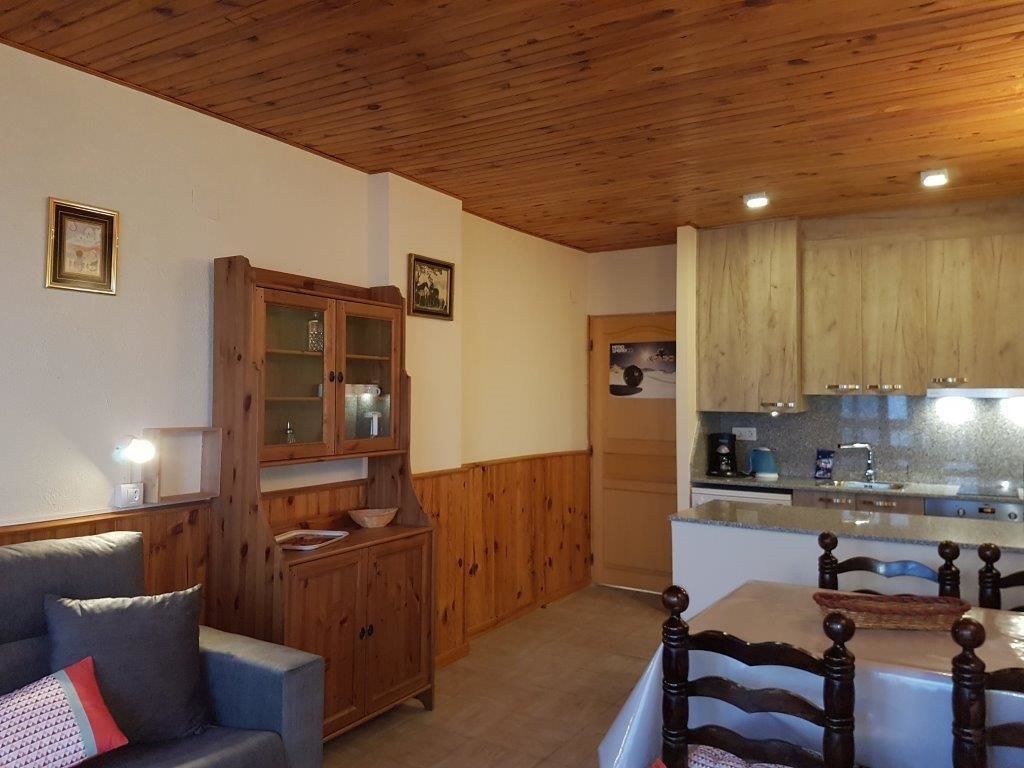 Una habitación acogedora con techo de madera, una mesa de comedor con sillas, un aparador de madera y una kitchenette con armarios de madera.