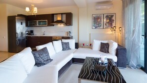 A modern living room with a sectional sofa, a coffee table, and a kitchen in the background. - White Rose Villa (Kassandra)