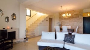 A modern living room with a white sofa, a flat-screen TV, a fireplace, and a staircase leading to a dining area. - White Rose Villa (Kassandra)