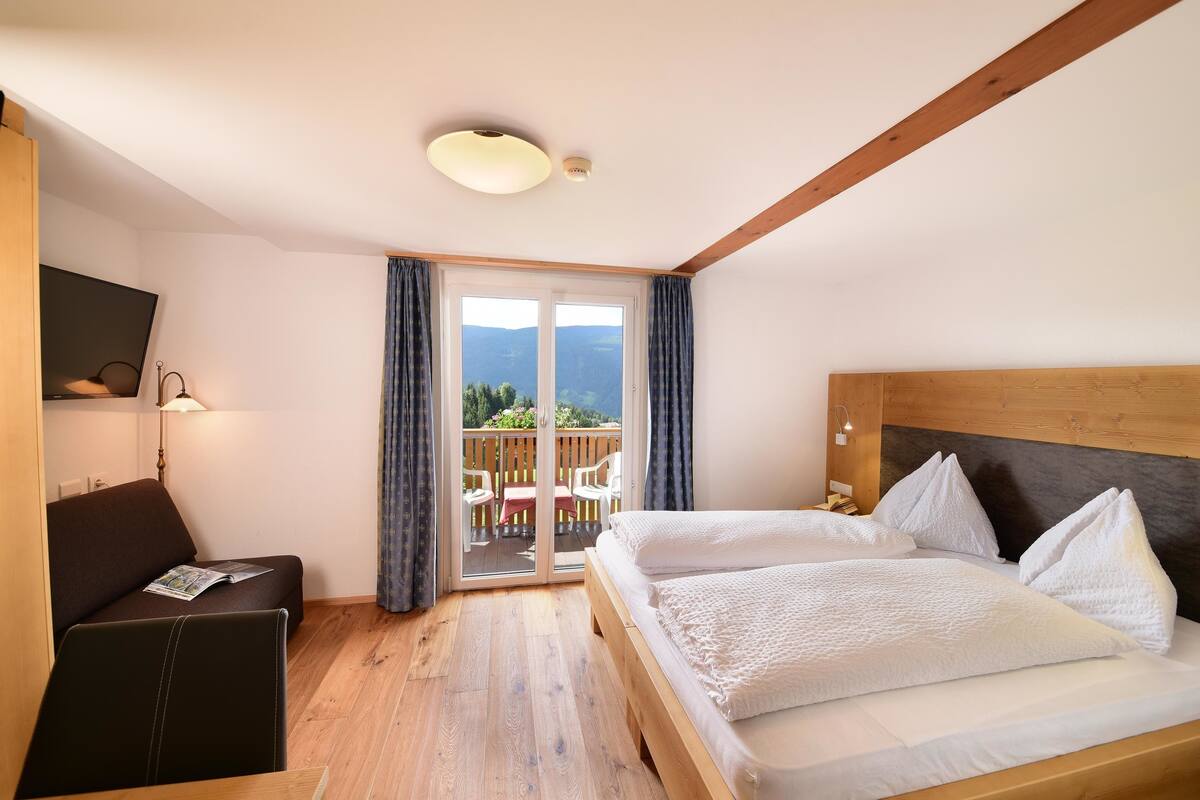 Une chambre d’hôtel comprenant un lit, un bureau, une chaise, une télévision et un balcon avec vue sur les montagnes.