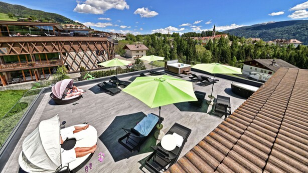 A rooftop terrace with sun loungers, umbrellas, and a pool area. - Hotel Tirolerhof (Terento)