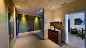 A modern hotel lobby with a glass partition, a wooden cabinet with towels, and a painting of a lake. - Hotel Tirolerhof (Terento)