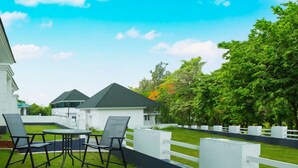 A white building with a covered patio area featuring a table and chairs, surrounded by a white fence and lush greenery. - Magic Land Resort (Chalakudy)