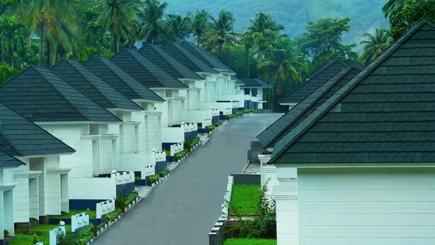 A row of white buildings with dark roofs, lined with greenery and palm trees in the background. - Magic Land Resort (Chalakudy)