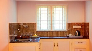 A kitchen with a window, wooden panel backsplash, and a sink with dishes and glasses. - Magic Land Resort (Chalakudy)
