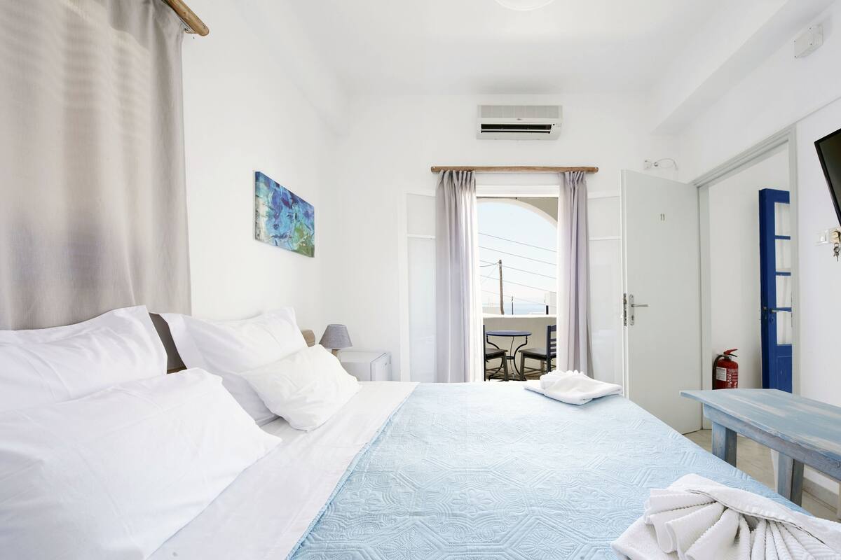 Habitación de hotel con cama, escritorio, silla, un cuadro y vistas al exterior.